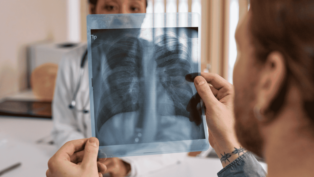 Hombre observando una radiografía de tórax en una consulta médica, con una doctora al fondo.